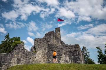 Schellenberg castle ruins with Liechtenstein flag Hiker in front of the historic ruins of Schellenberg Castle with a waving Liechtenstein flag under a blue sky